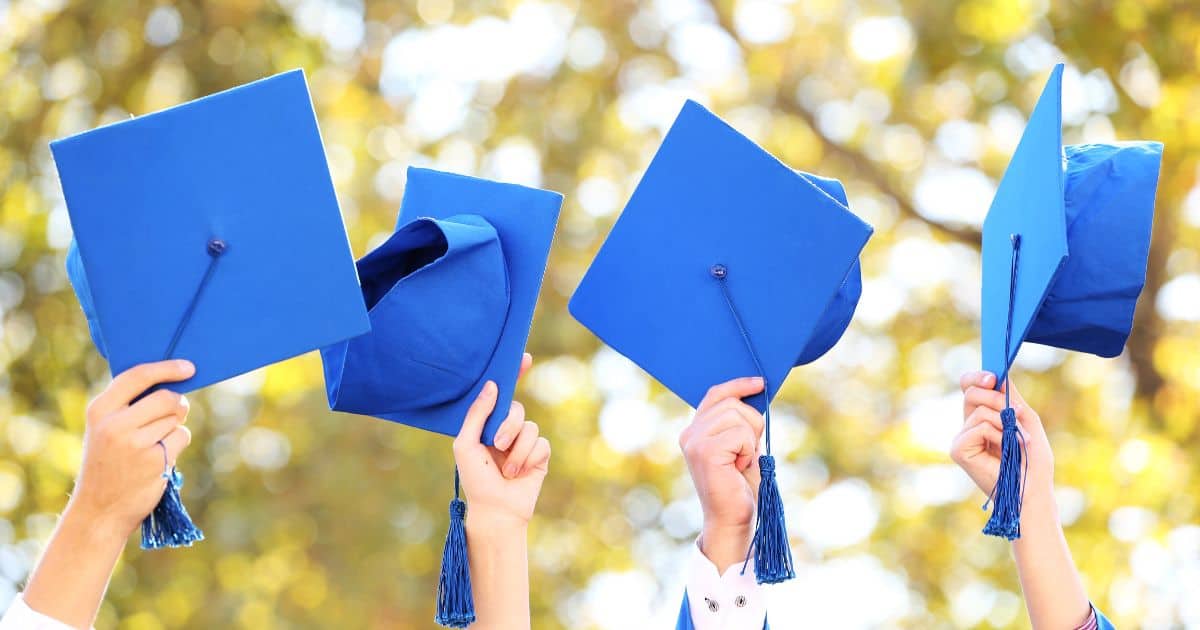 Four blue graduation caps raised in the air.