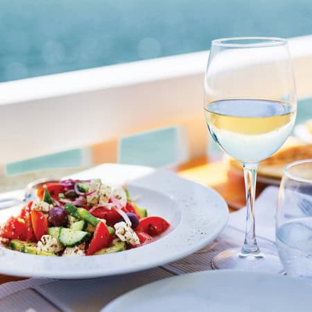 a wine glass and a salad plate sit on an outdoor table with a water view
