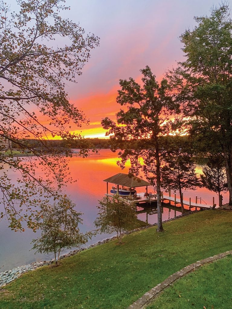 Brilliant red and golden sunset reflecting over Smith Mountain Lake, casting a warm glow on the water with a cozy boat dock in the foreground.