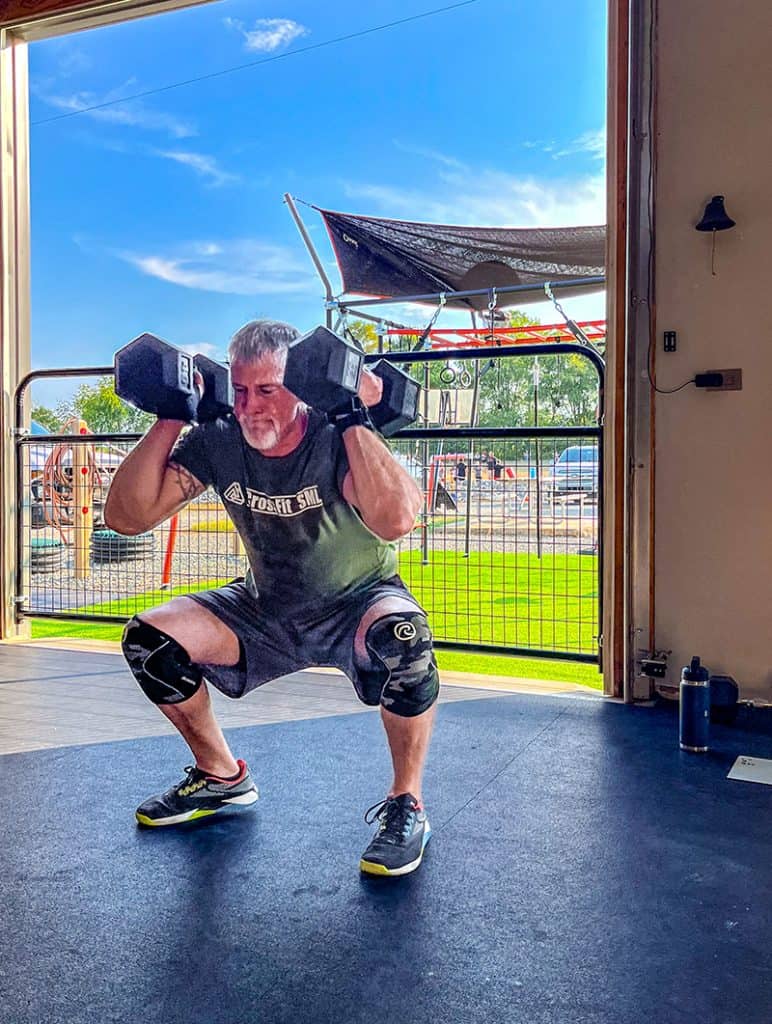 A person performs a squat exercise while holding two heavy dumbbells at shoulder height.