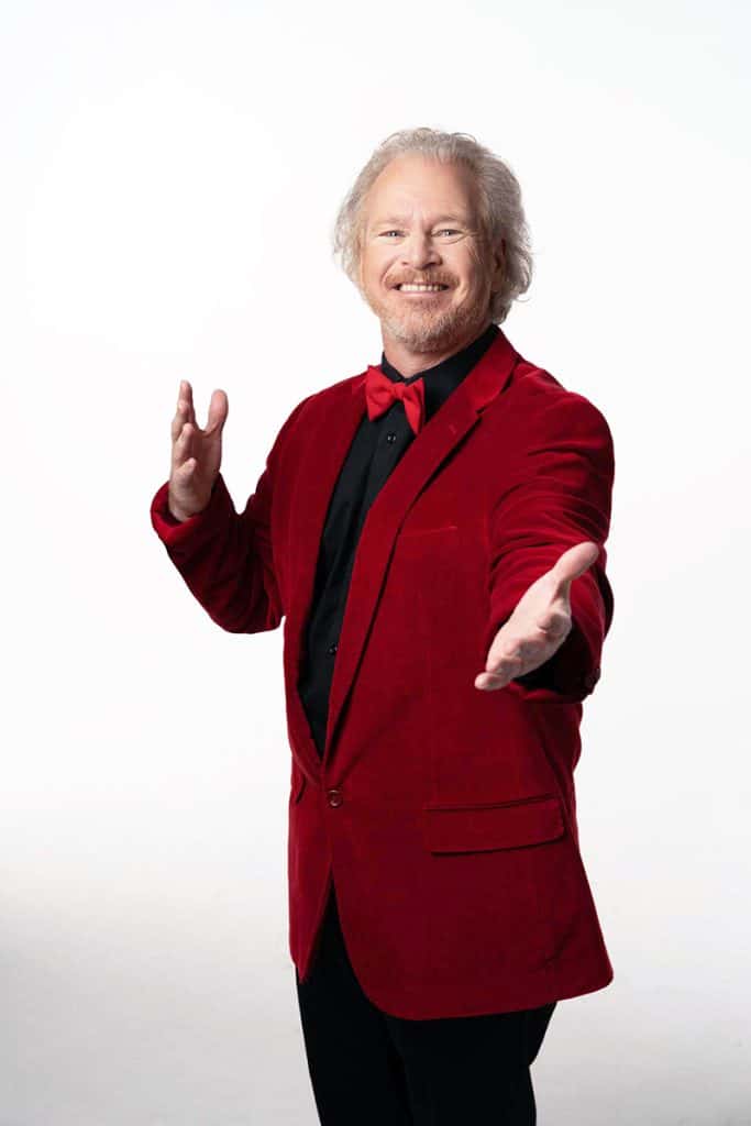 A man wearing a red velvet blazer and black bow tie stands against a white background.