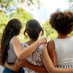 Three female friends hugging as seen from behind.