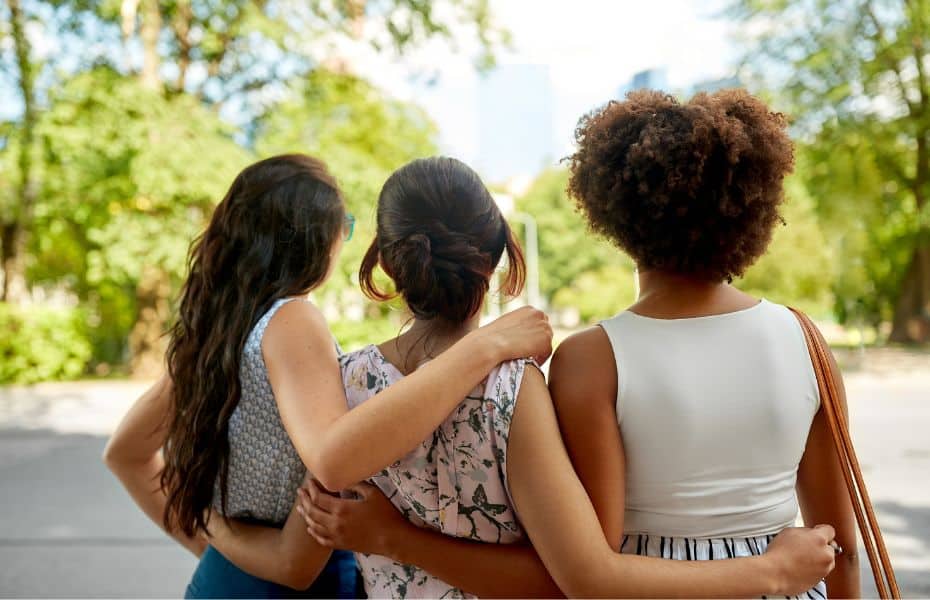 Three female friends hugging as seen from behind.