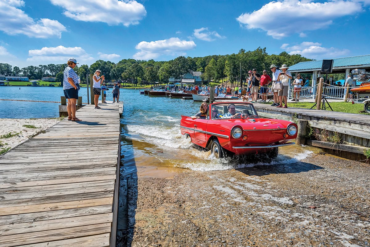 A bright red Amphicar drives out of the water onto a boat ramp at Smith Mountain Lake as spectators watch and take photos during the Antique and Classic Boat Show.