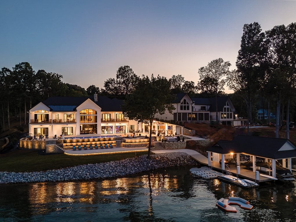 Modern Farmhouse style luxury vacation rental home lit up at night with lake in forground.