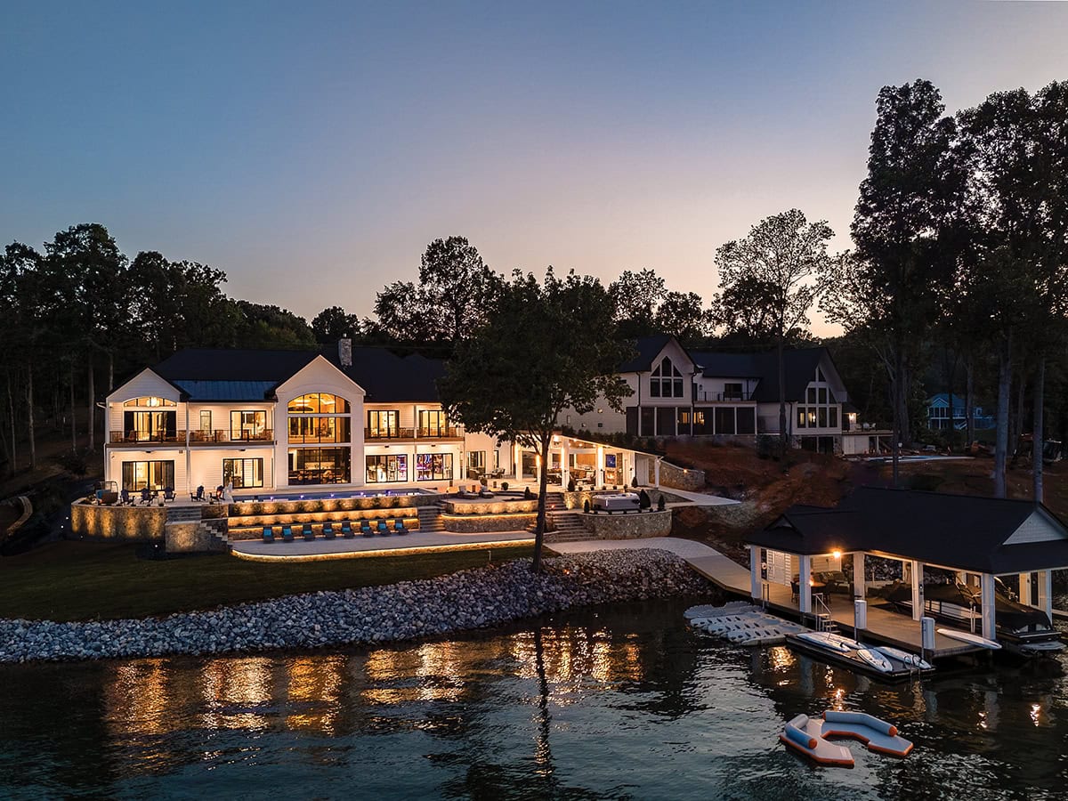 Modern Farmhouse style luxury vacation rental home lit up at night with lake in forground.