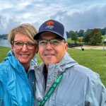 Andie and Chris Gibson selfie with rain jackets, a cloudy sky and Smith Mountain Lake Wine Festival background.