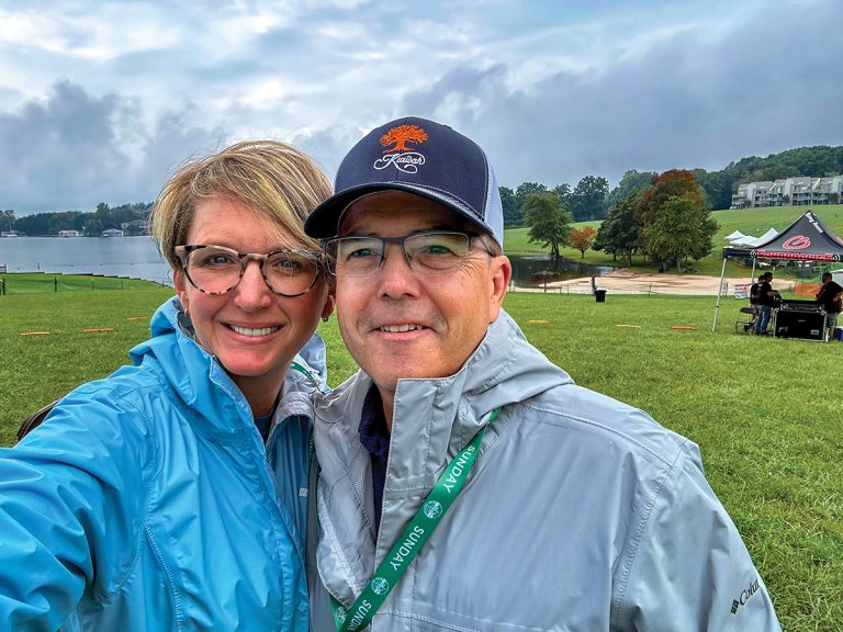 Andie and Chris Gibson selfie with rain jackets, a cloudy sky and Smith Mountain Lake Wine Festival background.