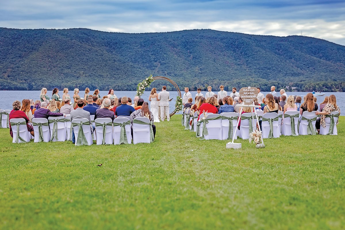 Outdoor wedding ceremony at Parkway Marina with guests seated on lawn, Smith Mountain Lake and sailboat visible in background