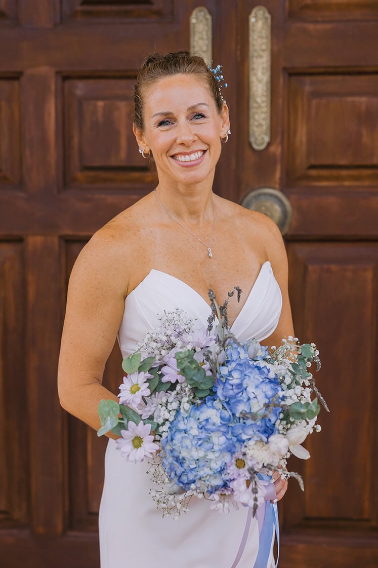 A bride stands on the brick porch at Smith Mountain Manor wedding venue holding her bouquet, photographed by Amative Creative