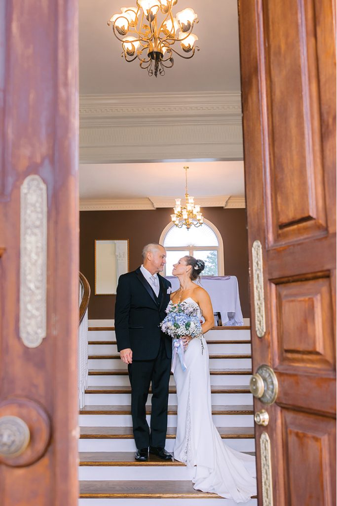 A bride and groom stand on the main staircase at Smith Mountain Manor wedding venue, photographed by Amative Creative