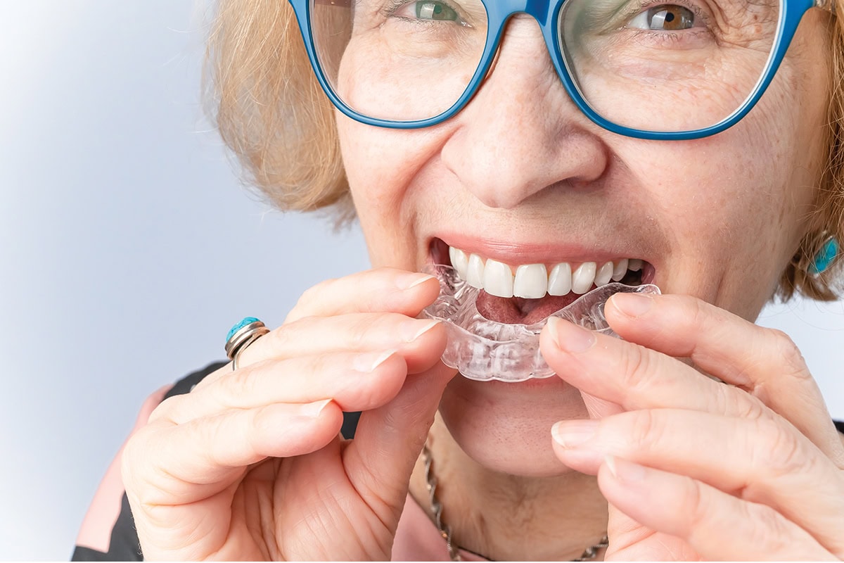 A happy elderly woman puts on transparent removable braces. Cosmetic dentistry for all ages
