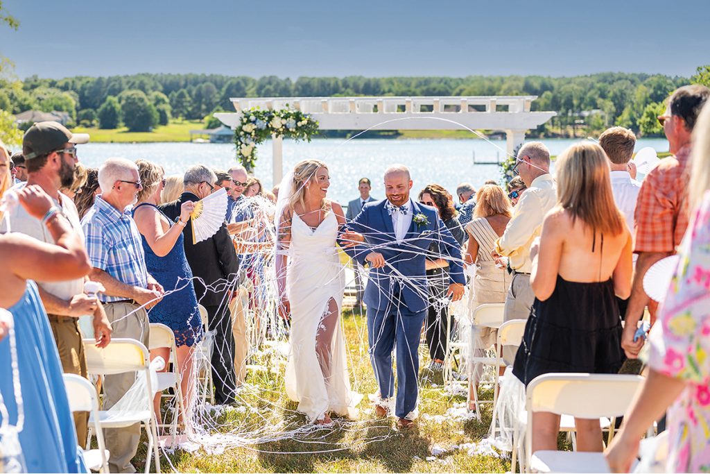 A bride and groom just married walking up the aisle with Smith Mountain Lake views at Bernard’s Landing, photographed by Suzanne Pfeiffer, Clark Street Photography
