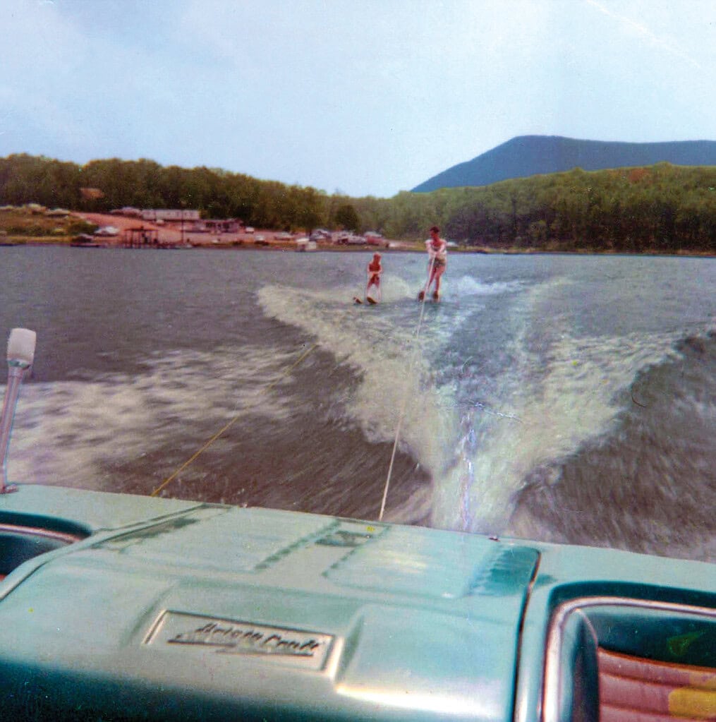 People enjoying water skiing and tubing on Smith Mountain Lake with scenic mountains and shoreline in the background.