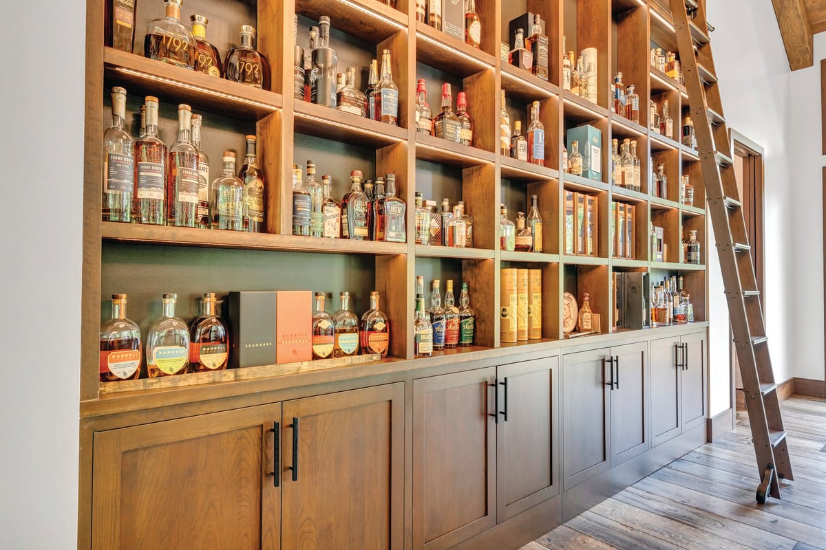 Wall of more than 150 bourbon bottles on shallow shelves with a rolling library ladder